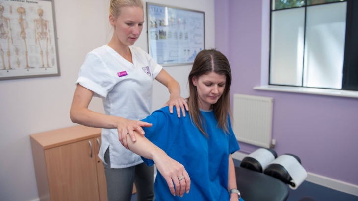 A female chiropractor treating a female patients arm and shoulder in a treatment room